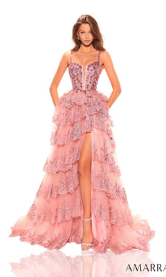 A woman wears the Amarra Sheer-Sides Long Ruffled Prom Dress 88745—an A-line pink evening gown with layered tulle, sequin details, spaghetti straps, and a high slit—while posing against a white background.