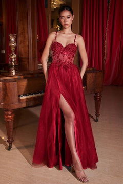 A woman stands indoors in front of a piano, wearing the Glitter-Tulle Long Prom Dress: Ladivine CD0234 with a lace-up bodice, thigh-high slit, and floral details. Red curtains and wood accents create an elegant backdrop.