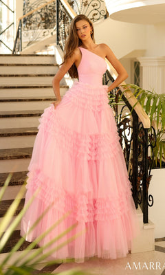 A woman poses elegantly by an indoor staircase with black railings, wearing the Amarra One-Shoulder Long Ruffled Prom Gown 88863—a floor-length pink dress with a ruffled skirt.