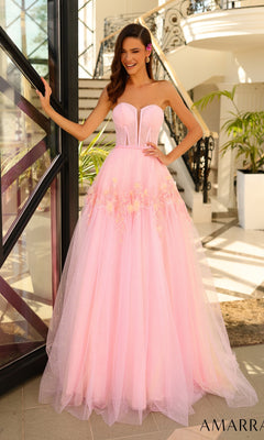 A woman wearing the Amarra Strapless Long Glitter Prom Ball Gown 88874 with floral details and a corset-style bodice stands indoors near stairs and glass doors, smiling with one hand on the doorframe.