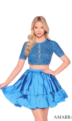 A woman with long blonde hair models the Amarra 88902, a blue short two-piece party dress with an embellished bodice and shiny ruffled A-line skirt, posing against a white background.