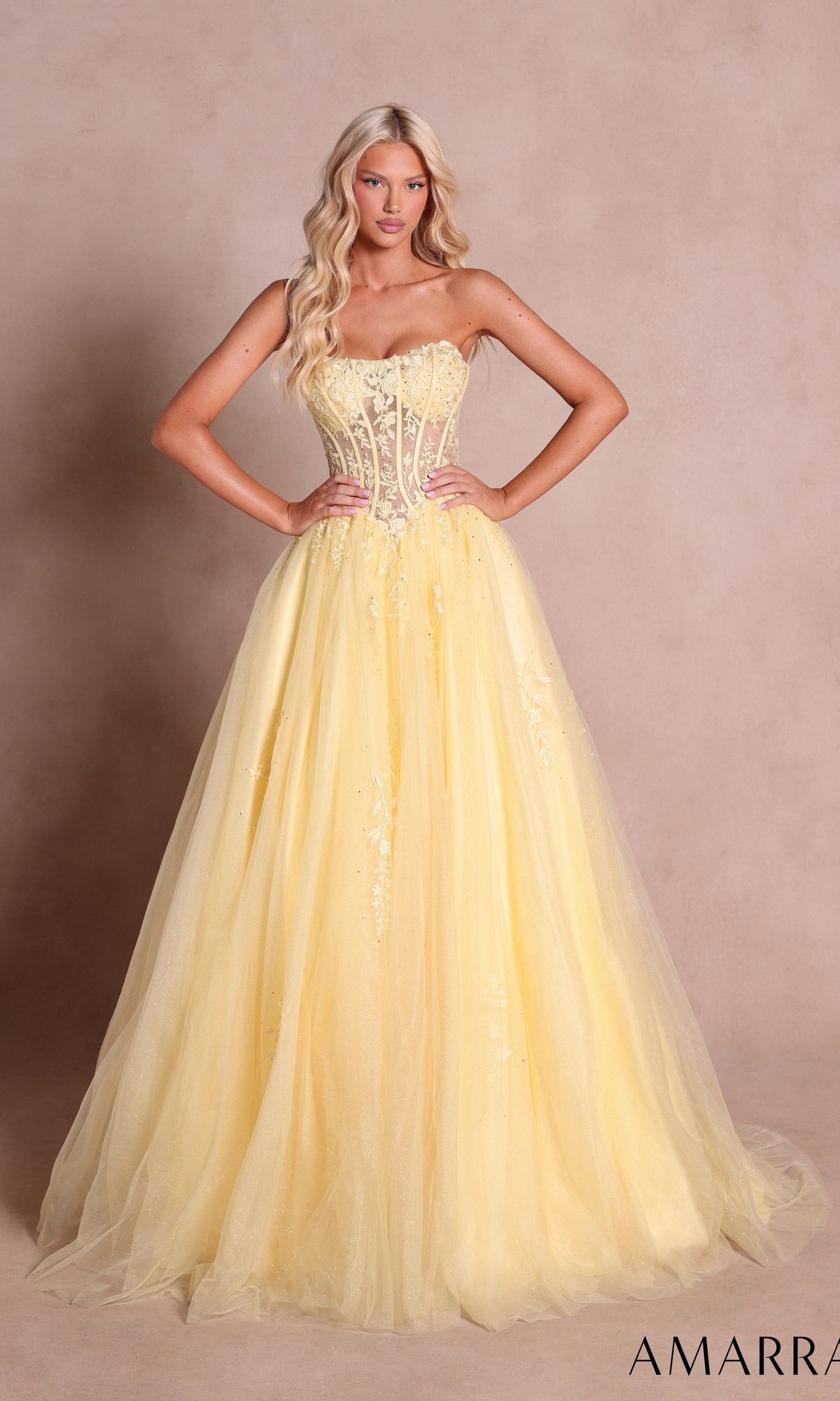 A woman stands with hands on hips, wearing the Amarra 88913 strapless long prom ball gown in light yellow—featuring a fitted, embellished bodice and a full tulle skirt.