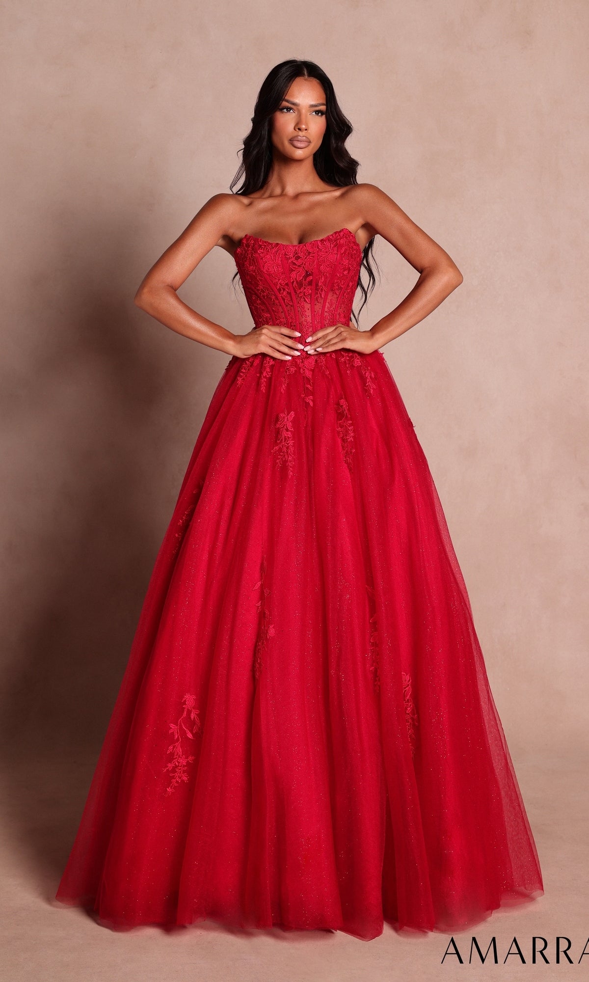 A woman stands gracefully in the Amarra 88913 Strapless Long Prom Ball Gown—a stunning, floor-length red ball gown adorned with intricate floral details and a sheer lace corset—elegantly posing against a neutral background. The word “AMARRA” appears in the bottom right corner.