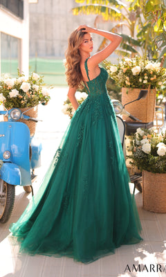 A woman in the Amarra 88970 long prom dress, a sleeveless green a-line gown, poses outdoors with one hand in her hair beside blue scooters and bright flower arrangements.