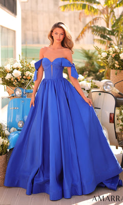 A woman in a bright blue Amarra 88995 Lace-Up Off-Shoulder Prom Ball Gown poses outdoors beside a blue Vespa scooter and elegant white flower arrangements.