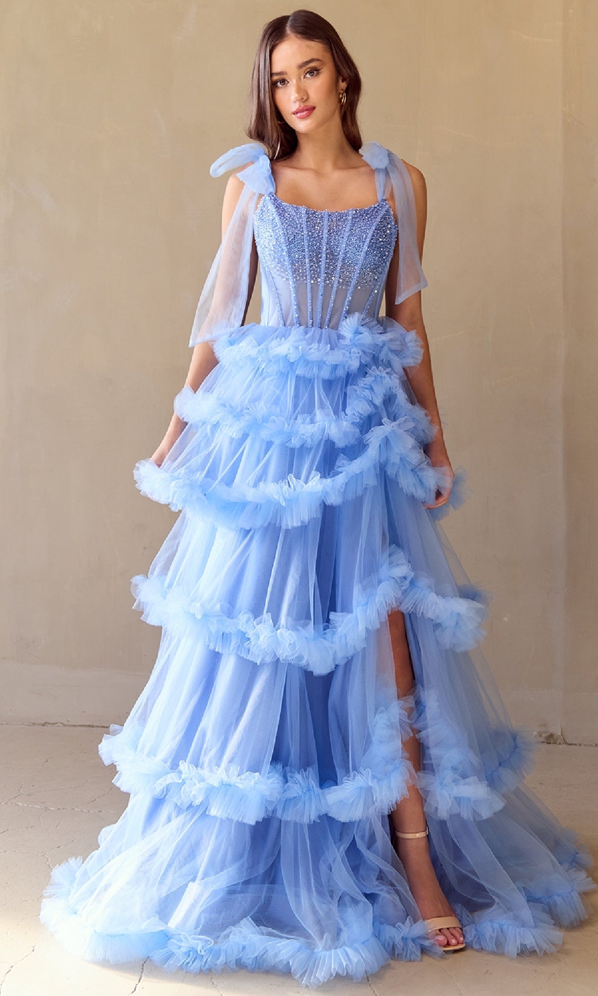 Woman wearing a light blue ball gown with ruffled layers on a plain background