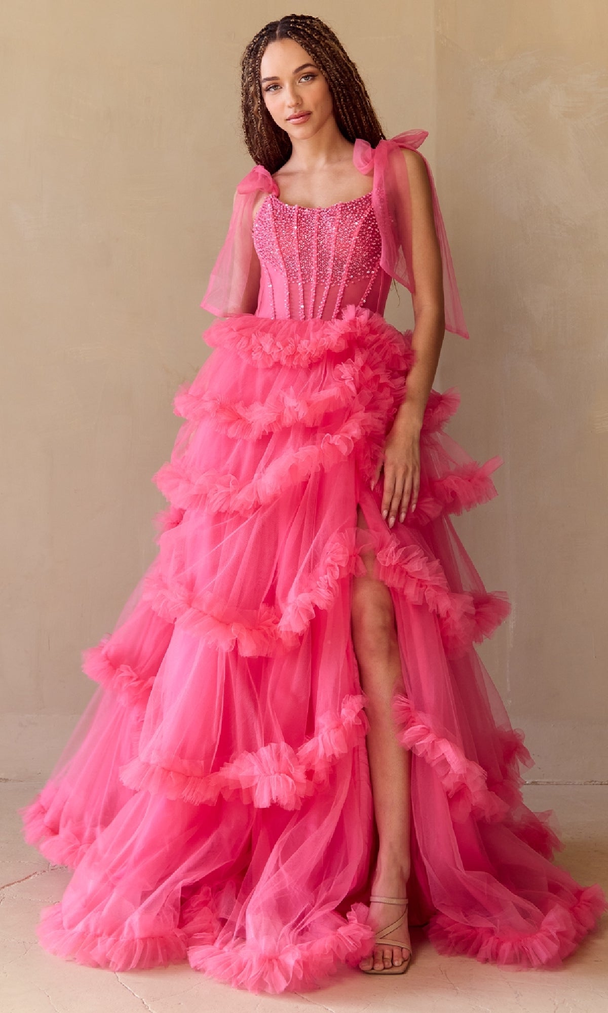 Woman wearing a pink ruffled ball gown against a beige background