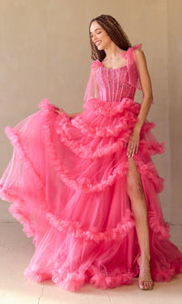 Woman wearing a pink ball gown with ruffled layers and a high slit on a plain background