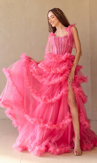 Woman wearing a pink ball gown with ruffled layers and a high slit on a plain background