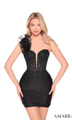 A woman models the Amarra 89005 One-Shoulder Mini Jersey Hoco Dress—black, form-fitting, with a sheer-lace bodice, deep V neckline, and large floral shoulder embellishment—against a white background.