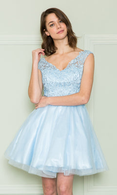 A woman wearing the Lace-Bodice Short Babydoll Homecoming Dress 8902, featuring a sleeveless light blue lace corset bodice and tulle skirt, stands against a pale wall and smiles softly at the camera.