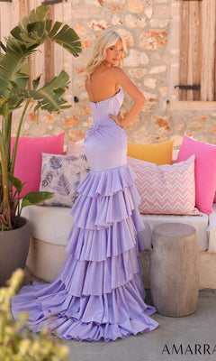 Wearing the Amarra 89058 long prom dress with a strapless corset bodice and tiered floor-length skirt, a woman stands outdoors by a stone wall, surrounded by vibrant plants and colorful pillows.