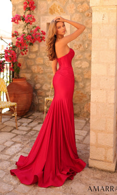 A woman poses outdoors in the Amarra 89062, a fitted strapless mermaid prom dress with an embellished sweetheart neckline, near pink flowers and a large clay pot on a stone patio.