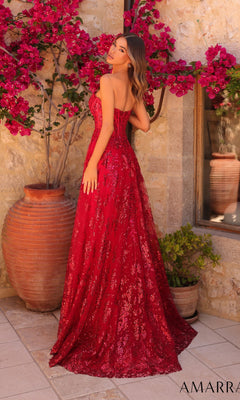 A woman wearing the Amarra 89074 long prom dress stands outdoors by a stone wall, with a large clay pot filled with pink flowers in the background.
