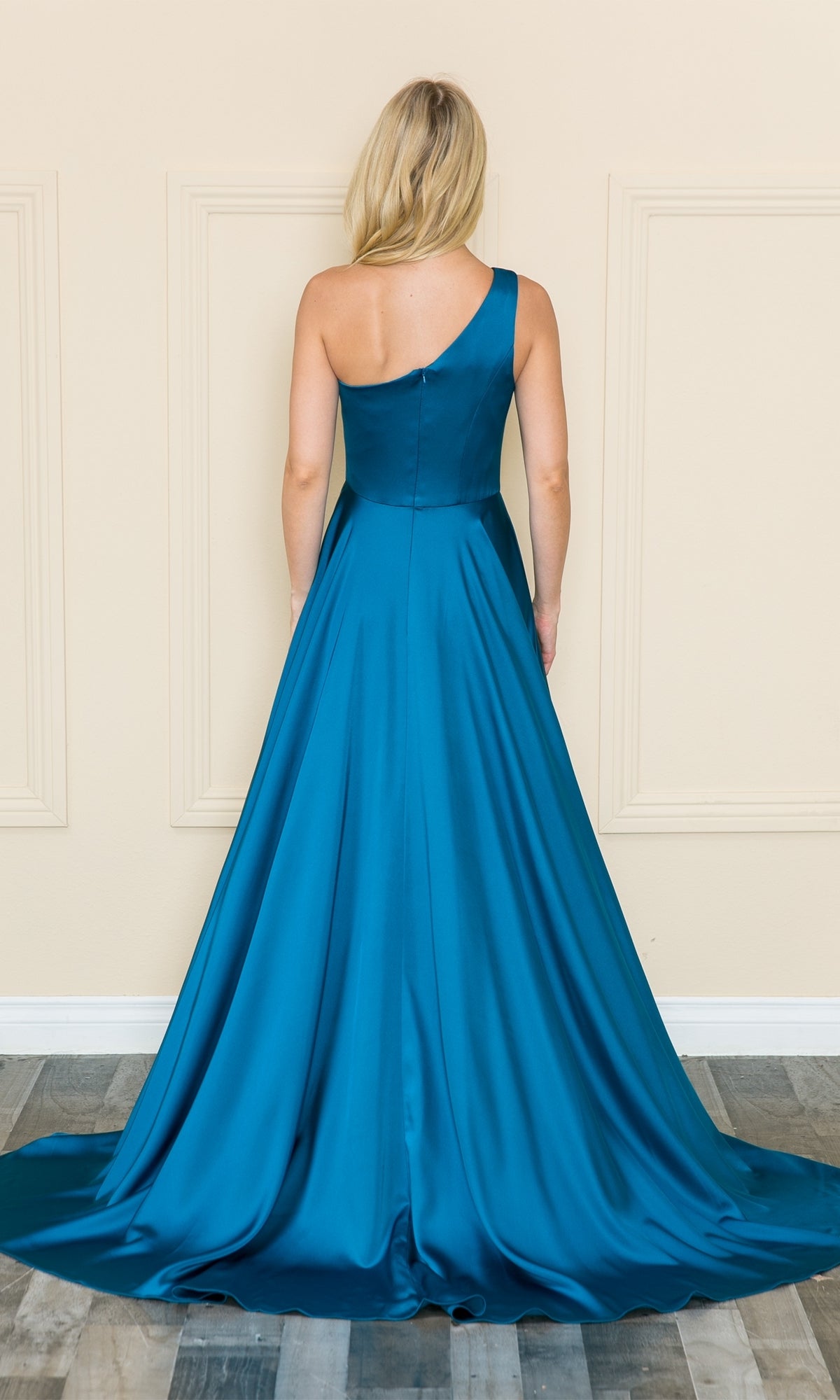 A woman stands facing away in the One-Shoulder Long Prom Dress with Pockets 8912—a floor-length teal satin gown with a slight train—in front of a cream-colored wall.