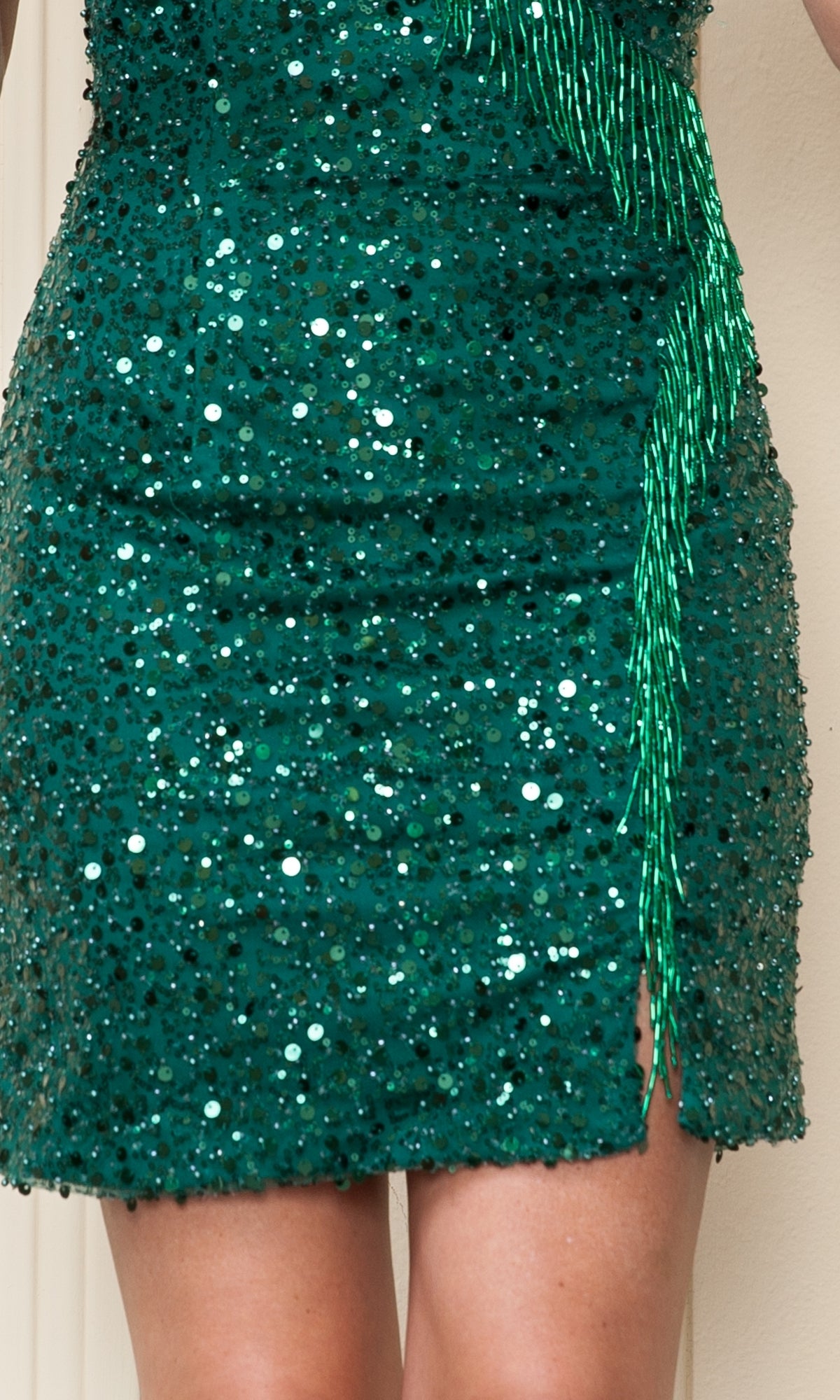 Close-up of a person wearing the Sequin Fringe Short Homecoming Dress 8926, a green strappy-back party dress with sequins, a thigh-high slit, and sparkling green beaded fringe detail.