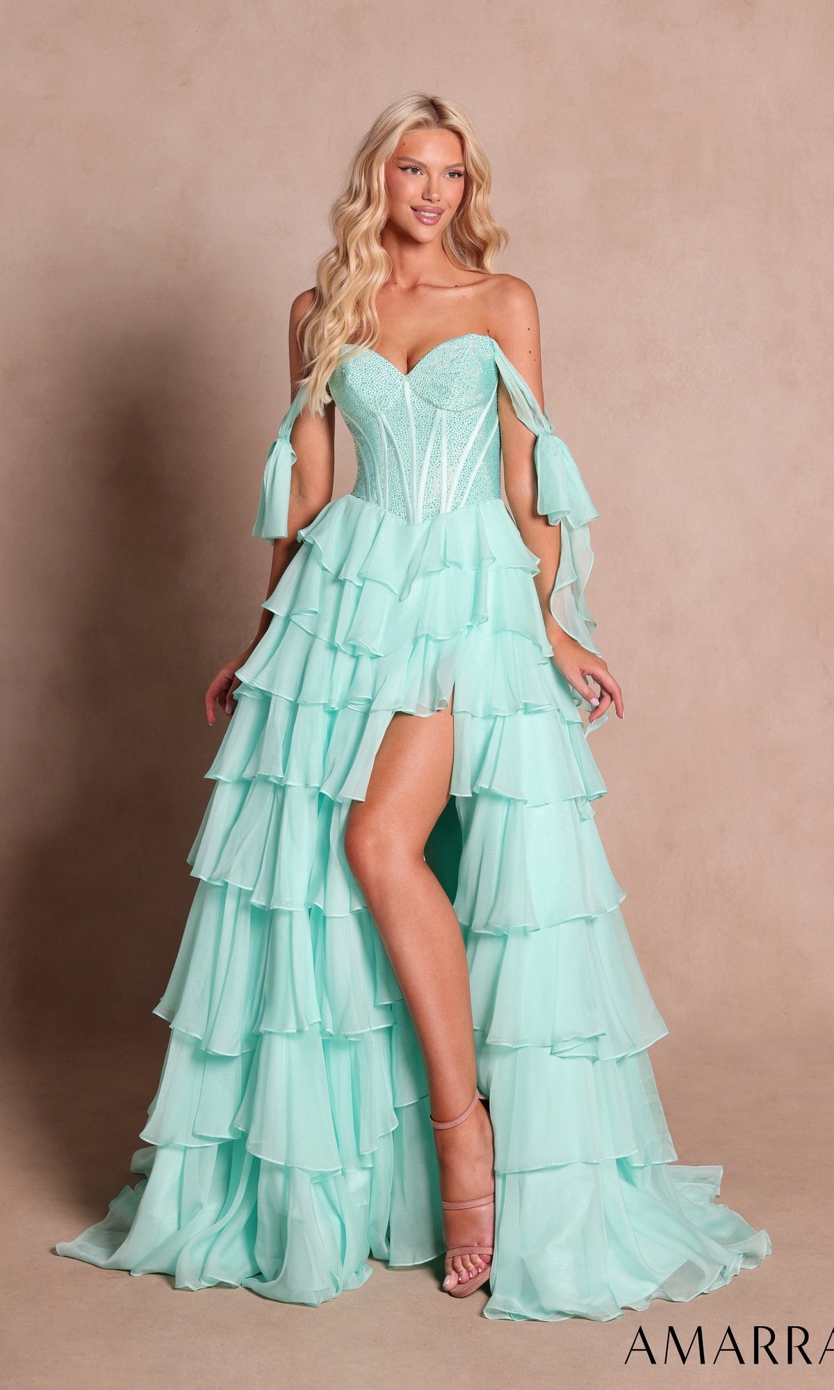 A woman stands against a plain beige background wearing the Amarra 89285 Long Prom Dress in mint—a strapless, ruffled gown featuring a tiered chiffon A-line skirt, an embellished corset bodice, and detached sleeves.