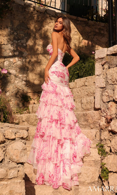 A woman in the Amarra 89297 long prom dress—strapless chiffon with pink floral ruffles—stands on stone steps outdoors, turned slightly away from the camera.