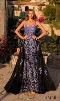 A woman stands outdoors in the Amarra 89373 long prom dress, a sleeveless black floor-length gown with a fitted silhouette, purple floral embroidery, and a floral-embellished tulle overskirt.