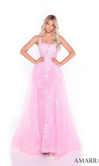 A woman stands with hands on hips against a white background, wearing the Amarra 89373 long prom dress—featuring a fitted silhouette, floor-length pink gown, and floral-embellished tulle overskirt with a sheer overlay.