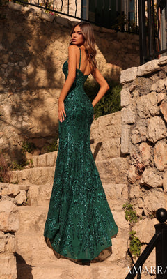 Wearing the Amarra 89453 long prom dress, a woman stands on stone steps outdoors in a green, patterned, floor-length gown with a sheer corset bodice, looking over her shoulder.