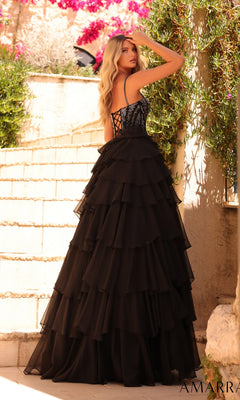 Wearing the Amarra 89459 Lace-Up Long Tiered Prom Dress, a woman stands on outdoor steps amidst greenery and flowers, glancing over her shoulder.