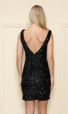 A woman with blonde hair wears the Short Velvet Sequin Homecoming Dress 8946, a sleeveless black party dress with a deep V-back, standing against a cream-colored wall.