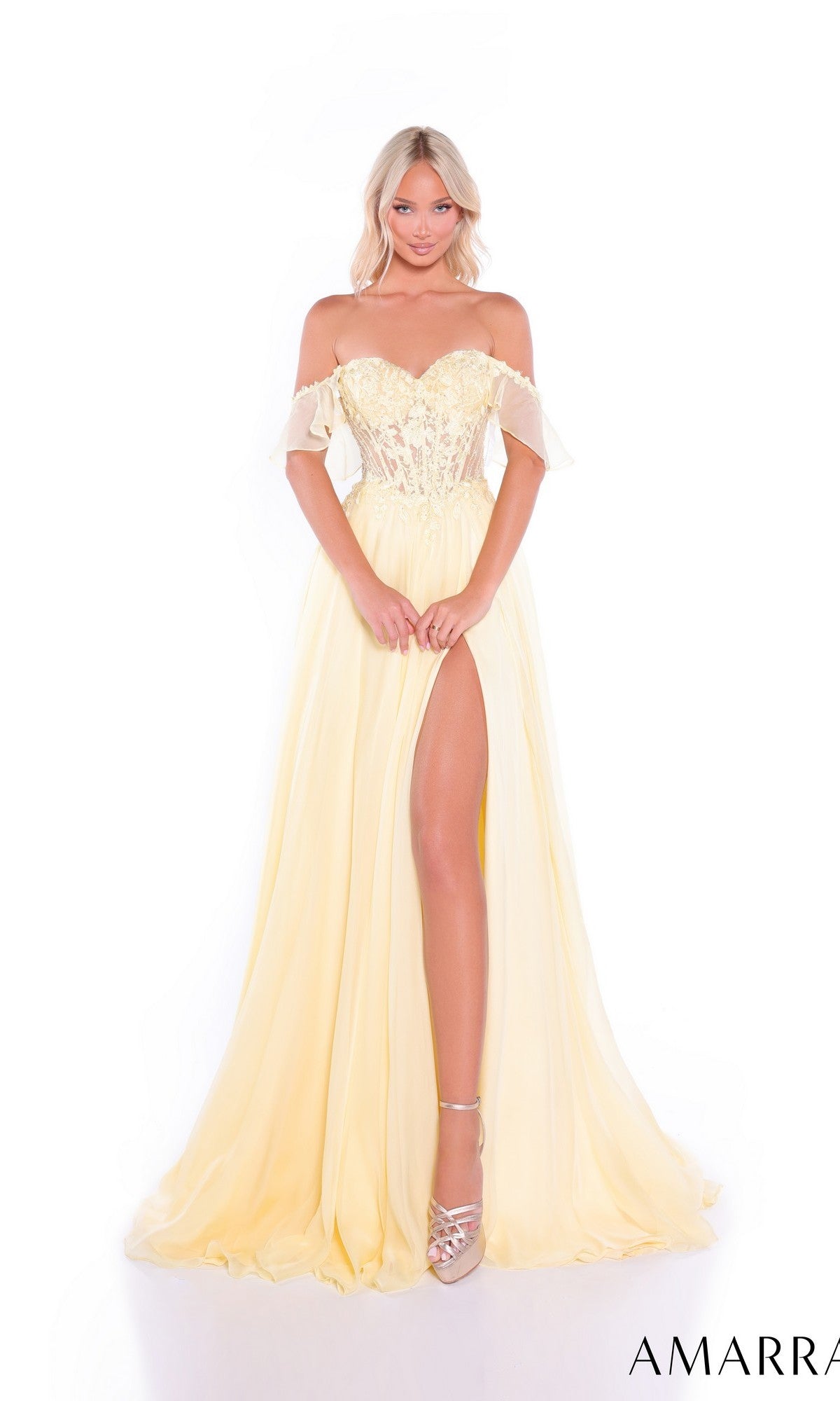A woman stands against a white background in the Long Prom Dress: Amarra 89481, a light yellow off-the-shoulder gown with a lace corset bodice, high slit, and flowing chiffon skirt.