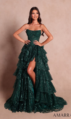 A woman wearing the Strapless Ruffled Prom Ball Gown: Amarra 89483 in emerald, featuring sequin tiered layers and a high slit, stands against a plain beige background.