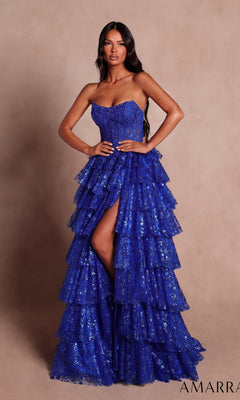 A woman wearing the Strapless Ruffled Prom Ball Gown: Amarra 89483 in royal blue, featuring a strapless neckline, dramatic ruffled tiers, and a high slit, stands against a plain beige background.