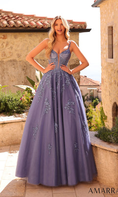 A woman poses outdoors in sunlight, wearing the Amarra 89493 Lace-Up Long Corset Prom Ball Gown in slate blue, surrounded by stone buildings and greenery.