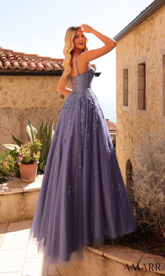 Wearing the Amarra 89493 Lace-Up Long Corset Prom Ball Gown, a woman stands outdoors by stone buildings and potted plants.