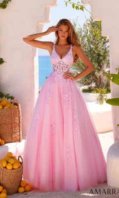 A woman in the Amarra 89523 Sheer-Waist Long A-Line Prom Dress in light pink, featuring floral lace embroidery, stands outdoors surrounded by white walls, baskets of lemons, and lush greenery.