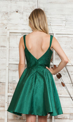 Woman in a Beaded Short A-Line Homecoming Dress 8958 stands facing a white wooden wall, with her right hand on her hip.