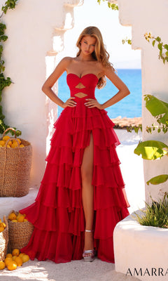 A woman stands outdoors by white walls, lemons, and greenery with the sea behind her, wearing the Amarra 89609 long prom dress featuring a strapless ruched bodice and tiered ruffle skirt.