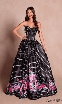 A woman wearing the Amarra 89624 long prom dress in Black/Print, a strapless ball gown with a corset bodice, decorated with white polka dots and pink floral print along the hem, stands against a neutral background.