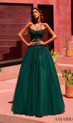 A woman wearing the Amarra 89627 long prom dress in emerald, featuring a strapless design with beaded floral lace details, stands outdoors near potted cacti and pink stucco steps.