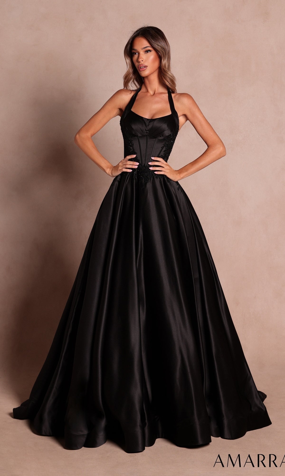 A woman wearing the Amarra 89646 long black prom dress, featuring a fitted bodice and halter neckline, poses against a neutral background.