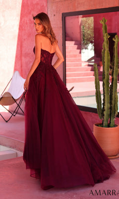 A woman wearing the Amarra 89689 long prom dress, a strapless floor-length burgundy gown, stands outdoors near a large potted cactus with her back to the camera.