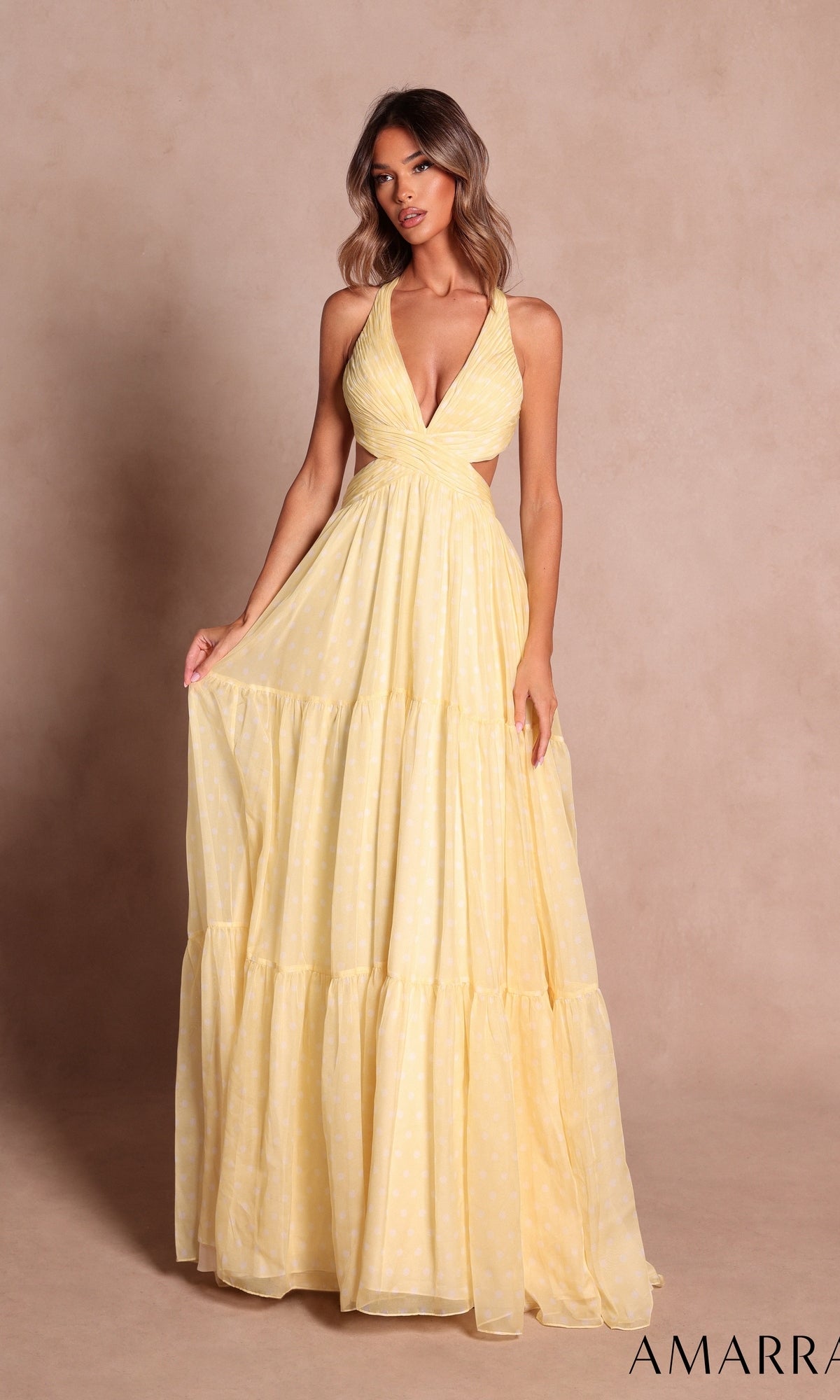 A woman wearing the Amarra 89730, a sleeveless, light yellow long prom dress with a halter neckline and tiered skirt, stands against a plain beige background.
