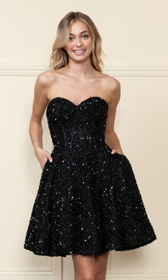 A woman smiles at the camera in the Strapless Sequin A-Line Homecoming Dress 8974, featuring black sequins, a fitted bodice, and flared skirt as she stands against a beige wall.