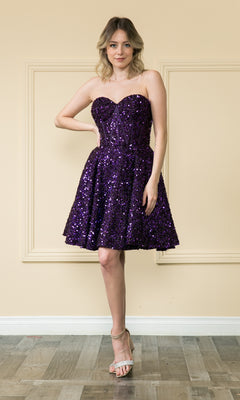 A person poses indoors wearing the Strapless Sequin A-Line Homecoming Dress 8974 in purple, styled with silver high-heeled sandals and posing confidently with one hand on their hip.