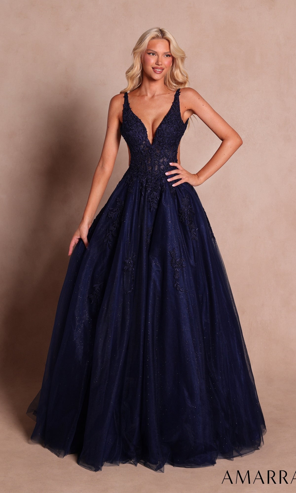 A woman wearing the Amarra 89786 long prom dress in navy, a floor-length gown featuring delicate floral lace appliqués and a deep V-neckline, standing against a neutral background.