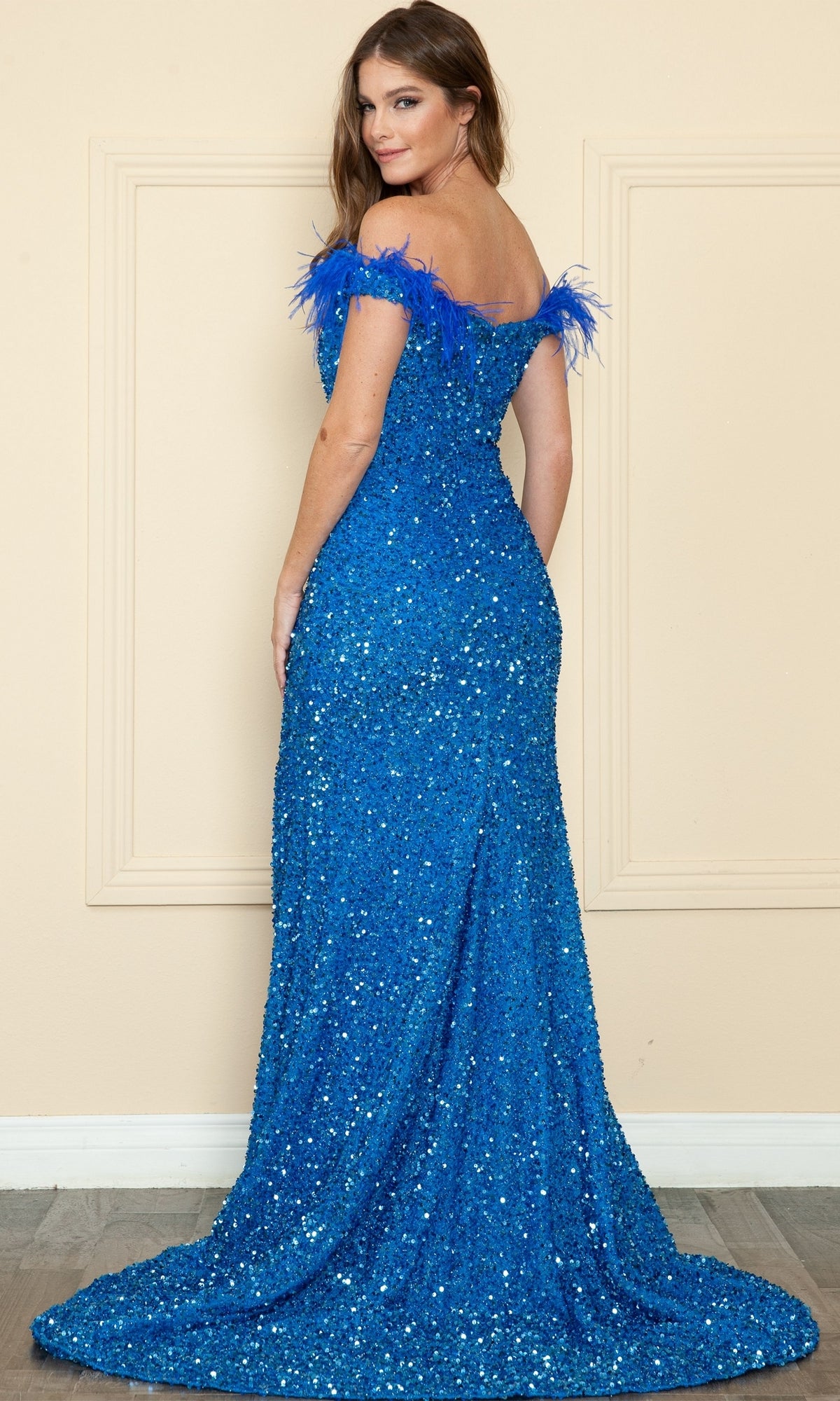 A woman in the Sequin-Velvet Long Feathered Prom Dress 8980, a floor-length, off-the-shoulder gown with sequin velvet and feather accents, stands facing away while looking over her shoulder.