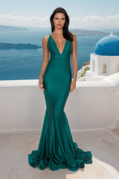 A woman in a fitted teal Strappy-Back Long Mermaid Prom Dress (Atria 6530H) stands on a white terrace with blue-domed buildings and the sea in the background.