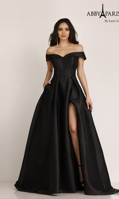 A woman stands against a plain background wearing the Classic Mikado Prom Ball Gown Abby Paris 90023—an off-the-shoulder, floor-length black dress with a thigh-high slit.