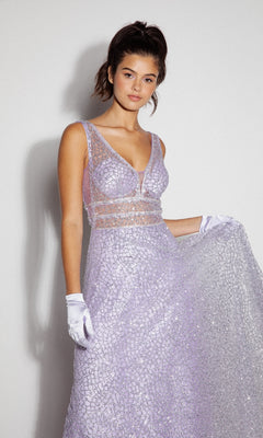 A young woman in the Sleeveless Long Glitter Formal Dress: Eureka 9005, featuring lilac sequins and sheer panels, stands against a plain background wearing white gloves and holding out the skirt of her gown.