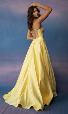 A woman in the Strappy-Back Long Satin Prom Dress: Eureka 9008 stands against a blue and purple backdrop, looking over her shoulder.