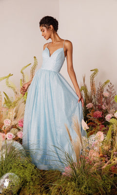 A woman in the Strappy-Back Glitter Prom Ball Gown: Eureka 9009, a light blue a-line dress with spaghetti straps, stands among flowers and greenery, holding one side of her gown.