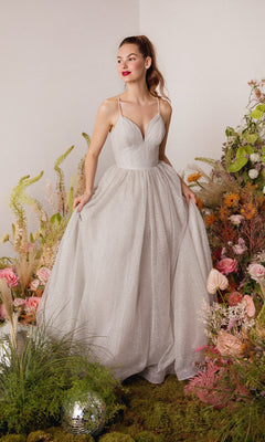 A woman in the Strappy-Back Glitter Prom Ball Gown: Eureka 9009 stands among colorful flowers and greenery, holding the sides of her sparkling gown.